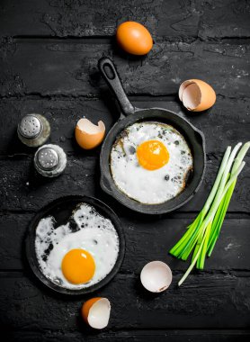 Sahanda yumurta yeşil soğan ve baharatlar ile. Rustik siyah arka plan üzerine.