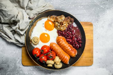 İngiliz kahvaltısı. Kızarmış yumurta sosis, domuz eti ve fasulye. Rustik bir arka plan üzerinde.