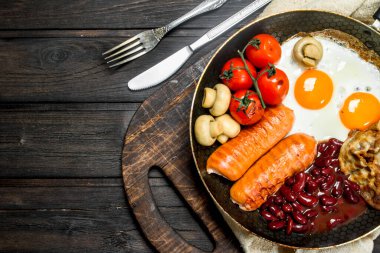 Geleneksel İngiliz kahvaltısı kızarmış yumurta, sosis ve fasulye. Ahşap bir arka plan üzerinde.