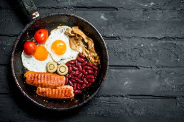 Bir tavada geleneksel İngiliz kahvaltısı. Rustik siyah arka plan üzerine.