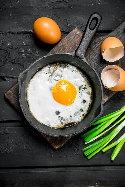 Stock image Fried egg with green onions and seasonings. On black rustic background.