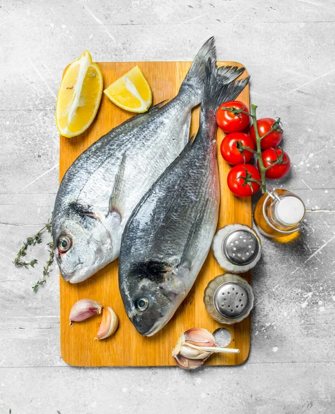 stock image Raw sea fish dorado with tomatoes, lemon wedges and spices. On a rustic background.