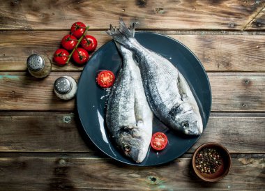 Çiğ deniz balığı dorado domates ve baharat bir tabakta. Ahşap bir arka plan üzerinde.