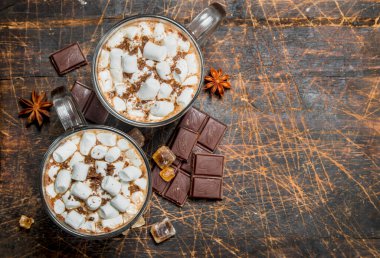 Sıcak çikolata şekerleme ve güzel kokulu tarçın ile kupalar içinde. Ahşap bir arka plan üzerinde.