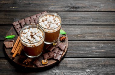 Sıcak çikolata şekerleme ve güzel kokulu tarçın ile kupalar içinde. Ahşap bir arka plan üzerinde.