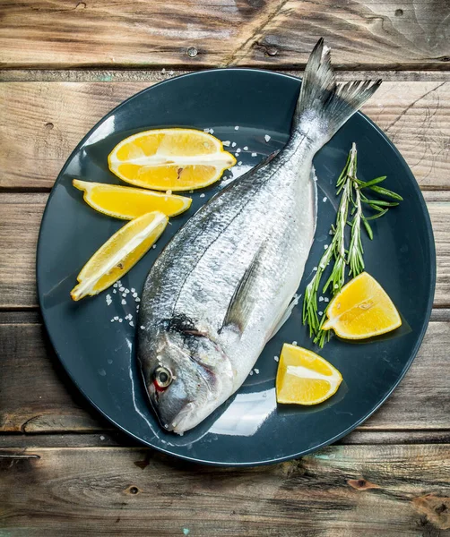 stock image Raw sea fish dorado with lemon on a plate. On a wooden background.