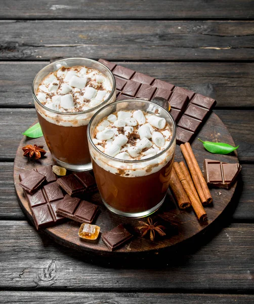 Sıcak çikolata şekerleme ve güzel kokulu tarçın ile kupalar içinde. Ahşap bir arka plan üzerinde.
