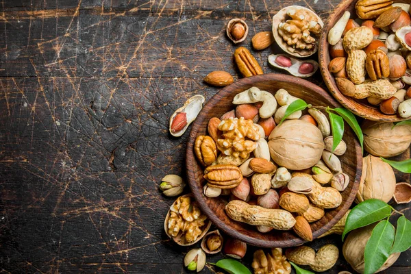 stock image Different types of nuts in bowls with green leaves. On a wooden background.