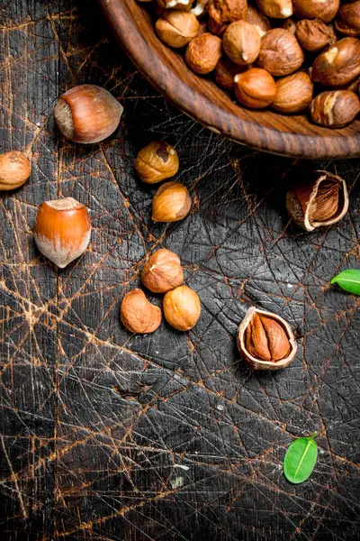 stock image Shelled hazelnuts with leaves in a bowl . On a wooden background.