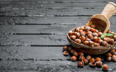 Ahşap bir kepçe ile bir kase fındık. Rustik siyah arka plan üzerine.