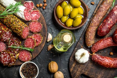 Zeytin, otlar ve baharatlar ile füme salam çeşitli. Rustik siyah arka plan üzerine.