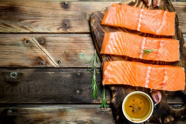 Biberiye ve zeytinyağı ile bir kesme tahtası üzerinde Çiğ somon balık biftek. Ahşap bir arka plan üzerinde.