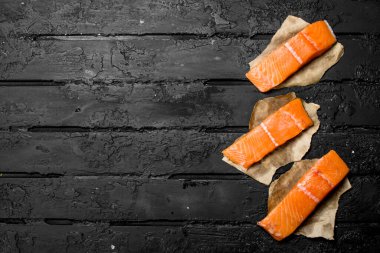 Çiğ somon biftek kağıt üzerinde balık. Rustik siyah arka plan üzerine.