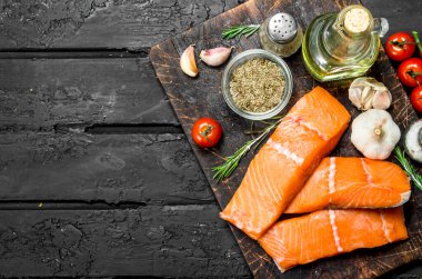 Çiğ somon fileto sarımsak, otlar ve domates ile balık. Rustik siyah arka plan üzerine.