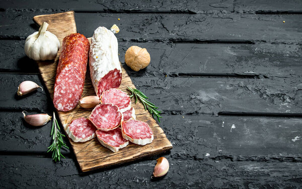 Salami with garlic and rosemary. On black rustic background.