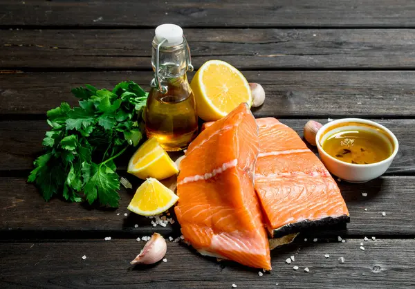 stock image Raw salmon fish filet with vegetables, spices and olive oil. On a wooden background.