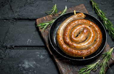 Güzel kokulu biberiye dalı ile kızarmış sosis. Rustik siyah arka plan üzerine.