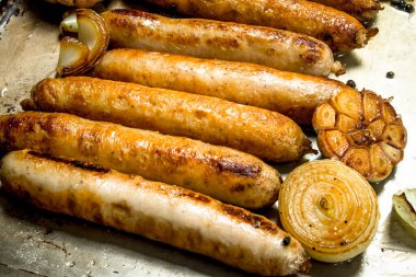 Sarımsak ve soğan ile kızarmış sosis. Fırın tepsisine.