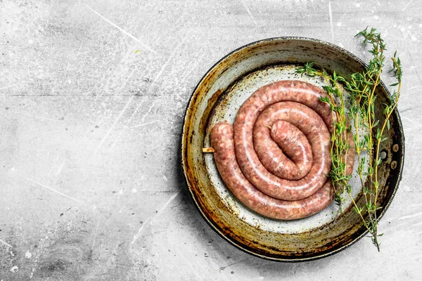 stock image Raw sausages in a pan with thyme. On a rustic background.