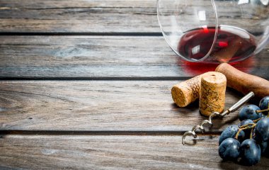 Şarap arka plan. Bir bardak kırmızı şarap ile bir tirbuşon ve bir asma. Ahşap bir arka plan üzerinde.