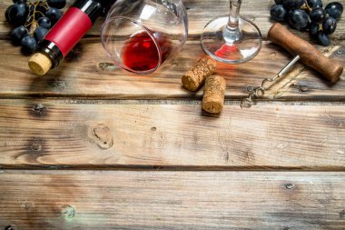 Kırmızı şarap bir bardak üzüm ve bir tirbuşon. Ahşap bir arka plan üzerinde.