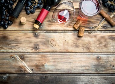 Kırmızı şarap bir bardak üzüm ve bir tirbuşon. Ahşap bir arka plan üzerinde.