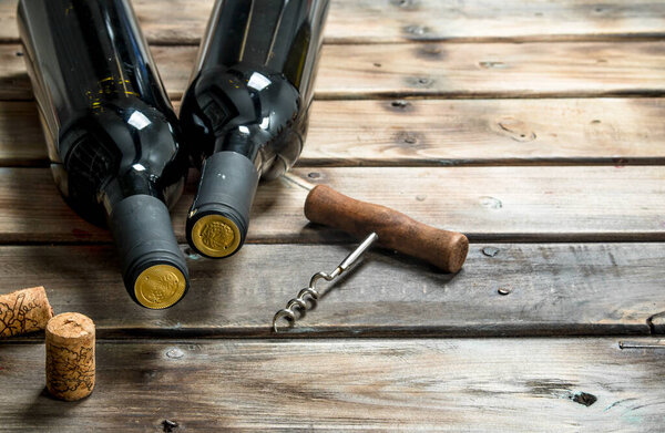 bottle of red wine with a corkscrew. On a wooden background.