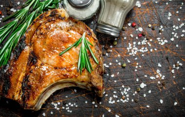 Bir dal taze biberiye ile kemik ızgara domuz biftek. Ahşap bir arka plan üzerinde.