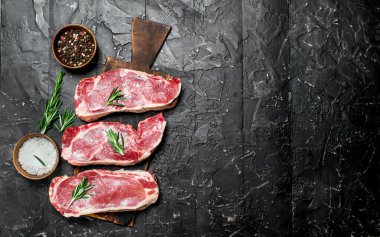 Ham mermer sığır biftek tuz ve baharatlar ile. Siyah bir rustik arka planda.