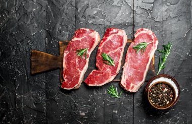 Ham mermer sığır biftek tuz ve baharatlar ile. Siyah bir rustik arka planda.