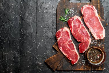 Ham mermer sığır biftek tuz ve baharatlar ile. Siyah bir rustik arka planda.