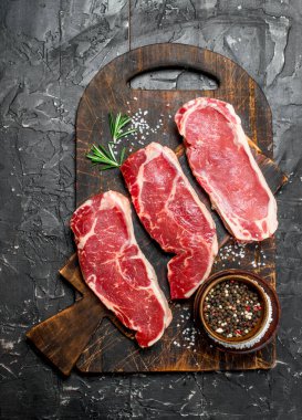 Ham mermer sığır biftek tuz ve baharatlar ile. Siyah bir rustik arka planda.