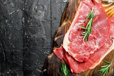 Ham sığır eti biftek güzel kokulu biberiye ile. Siyah bir rustik arka planda.