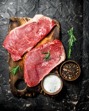 Ham mermer sığır biftek tuz ve baharatlar ile. Siyah bir rustik arka planda.