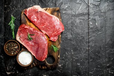 Ham mermer sığır biftek tuz ve baharatlar ile. Siyah bir rustik arka planda.