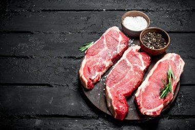 Ham sığır eti biftek baharatlar ile. Siyah bir rustik arka planda.