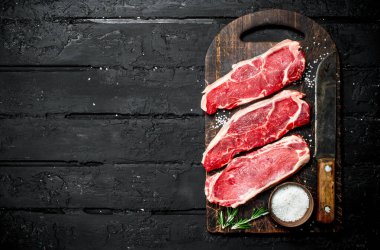 Çiğ biftek tuz ile sulu biftek. Siyah bir rustik arka planda.