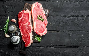 Baharatlar ve tuz ile ham sığır eti biftek. Siyah bir rustik arka planda.