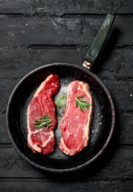 Biberiye delikanlı ile eski bir tavada ham sığır eti biftek. Siyah bir rustik arka planda.