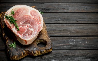 Kesme tahtası üzerinde rosemary ile büyük çiğ domuz biftek. Ahşap bir arka plan üzerinde.