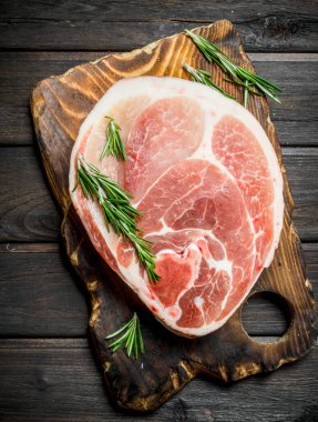 Kesme tahtası üzerinde rosemary ile büyük çiğ domuz biftek. Ahşap bir arka plan üzerinde.