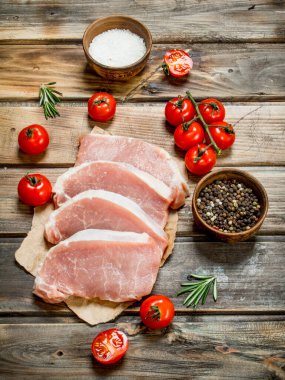 Çiğ domuz biftek domates ve biberiye ile. Ahşap bir arka plan üzerinde.