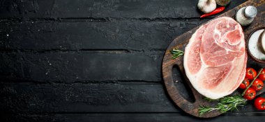 Büyük ham domuz biftek baharat ve sebzeler ile. Siyah bir rustik arka planda.