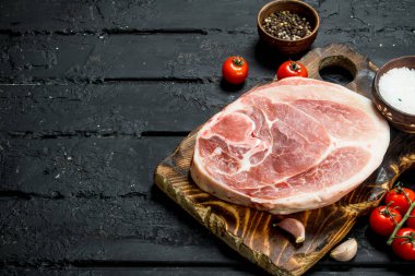 Büyük ham domuz biftek domates ve baharat. Siyah bir rustik arka planda.