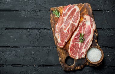 Çiğ domuz biftek aromatik ve otlar ve baharatlar ile. Siyah bir rustik arka planda.