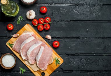 Çiğ domuz biftek domates ve baharat ile. Siyah bir rustik arka planda.