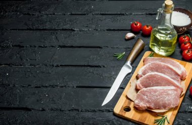 Çiğ domuz biftek domates ve baharat ile. Siyah bir rustik arka planda.