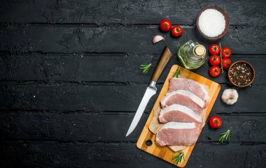 Çiğ domuz biftek domates ve baharat ile. Siyah bir rustik arka planda.