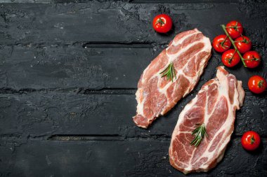 Çiğ domuz biftek domates ve biberiye ile. Siyah bir rustik arka planda.