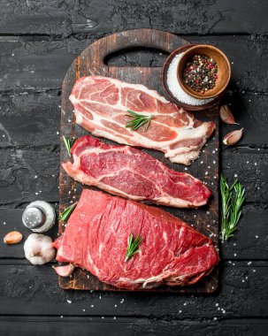 Çiğ et. Sığır eti ve domuz eti biftek kesme tahtası üzerinde baharatlar ile. Siyah bir rustik arka planda.